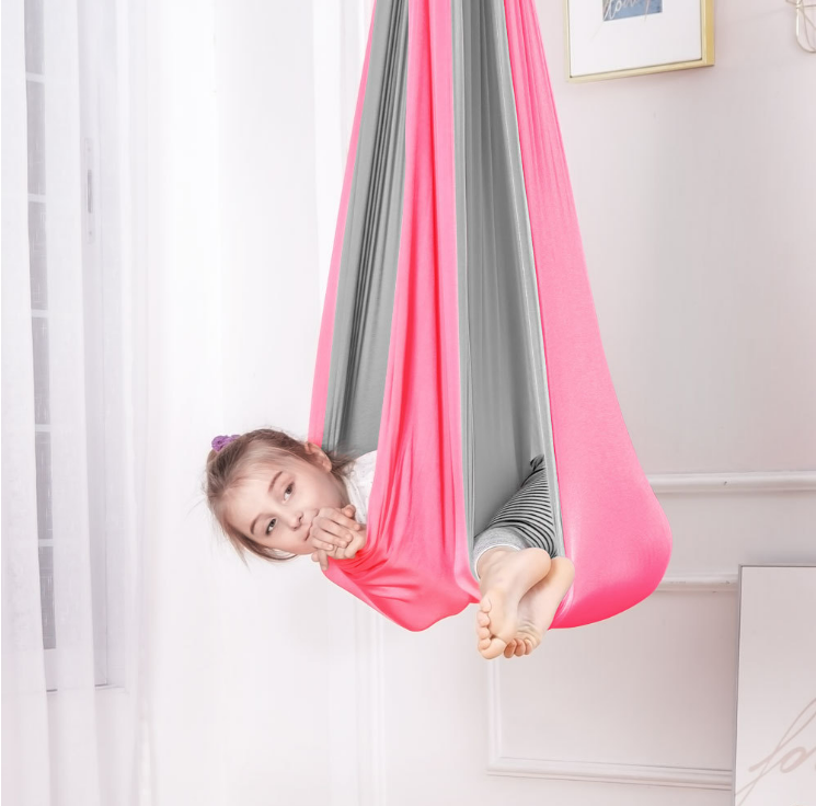 Kind liegt entspannt in einer bunten, hängenden Therapieschaukel im Kinderzimmer