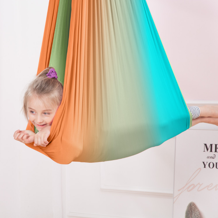Kind liegt entspannt in einer bunten, hängenden Therapieschaukel im Kinderzimmer
