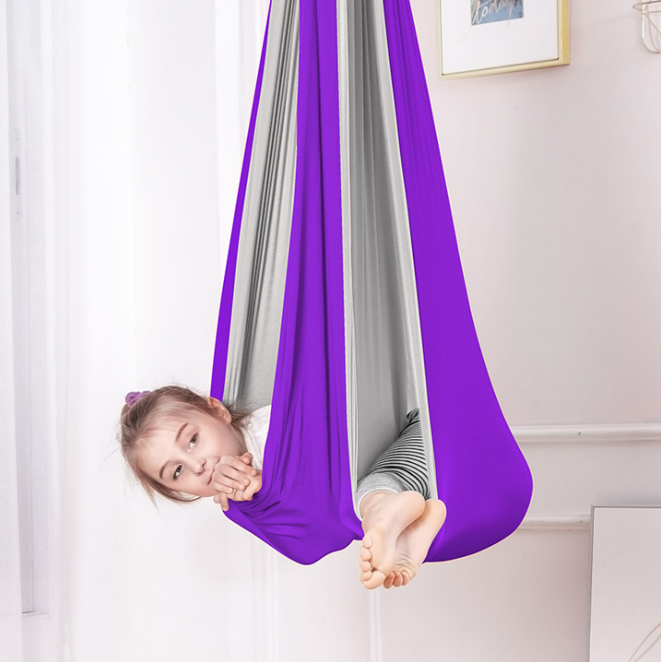 Kind liegt entspannt in einer bunten, hängenden Therapieschaukel im Kinderzimmer