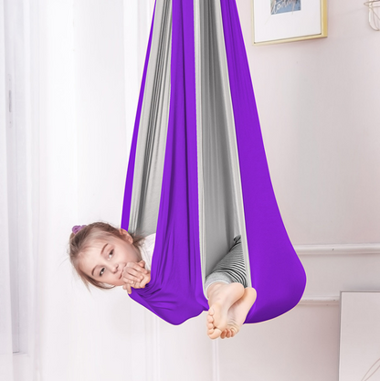 Kind liegt entspannt in einer bunten, hängenden Therapieschaukel im Kinderzimmer