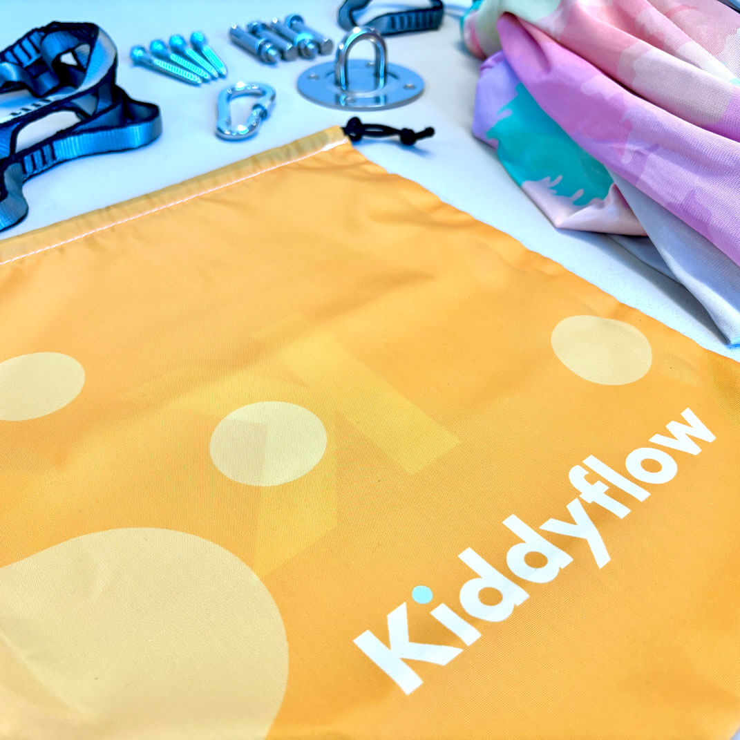 Detailaufnahme des Kiddyflow Aufbewahrungsbeutels mit Teilen des Lieferumfangs und der doppellagigen Flow Therapieschaukel 2.0 im Rainbow-Design.