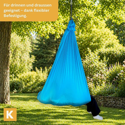 Kind entspannt draussen in hellblauer Kiddyflow Therapieschaukel  – aufgehängt an einem Baum.