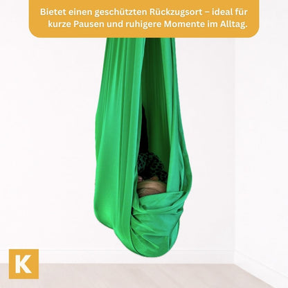 Kind geborgen in einer grünen Therapieschaukel von Kiddyflow im Innenbereich